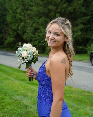 A bridesmaid in a royal blue lace dress holds a white and green floral bouquet at an outdoor event.