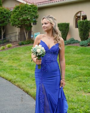 A formal event attendee poses in a fitted royal blue gown with lace details while holding a floral bouquet.