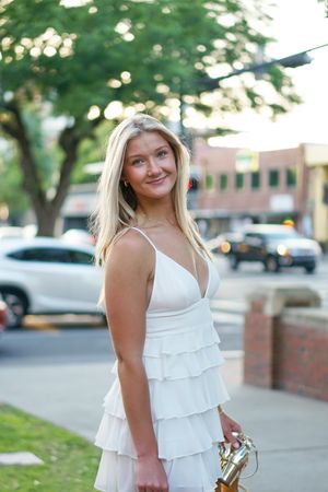 A person in a white tiered summer dress poses on a sidewalk during golden hour.