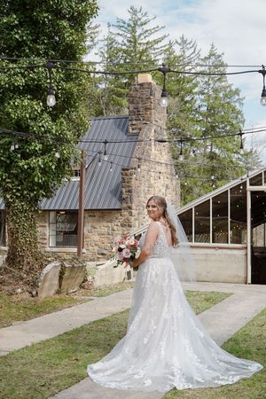 A stunning bridal portrait series showcasing a flowing white lace wedding gown with cathedral train against a rustic stone backdrop.