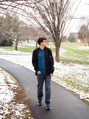 A casual winter scene of someone walking along a snowy path wearing a blue shirt and black jacket.