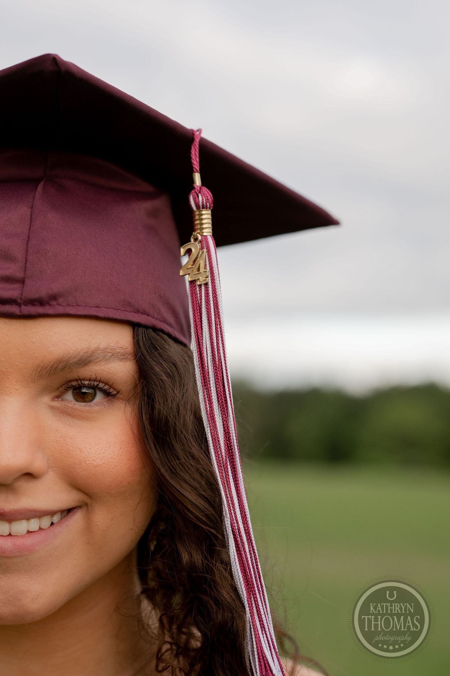 Close-up portrait showing burgundy graduation cap with tassel against green field background.