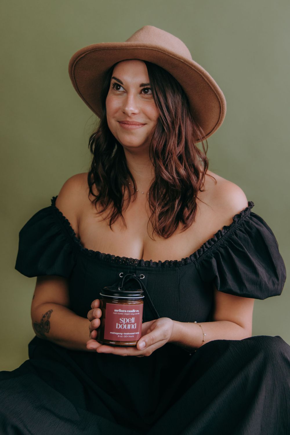 Lifestyle photo of a person in black dress and hat showcasing a skincare product jar.