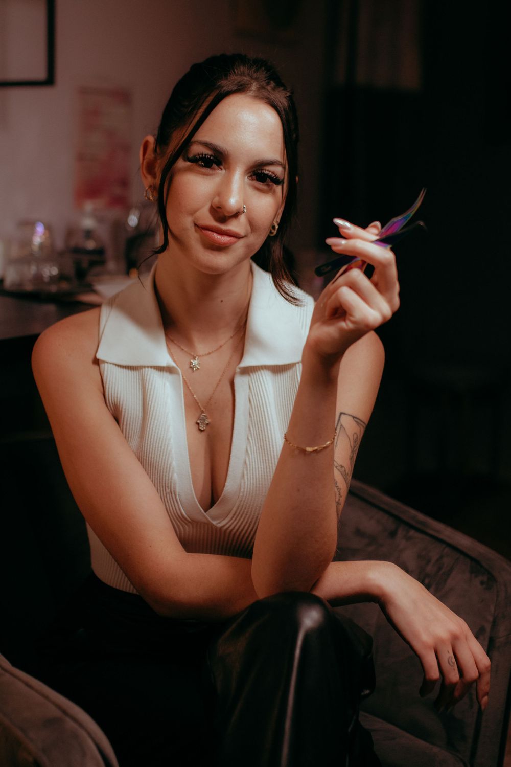 Beauty professional in white top holding tweezers while seated in salon chair.
