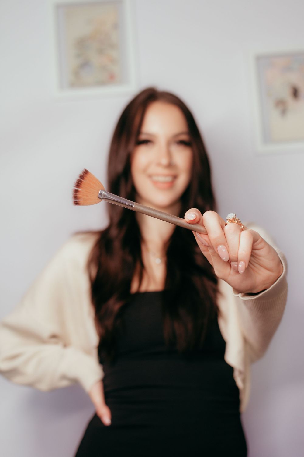 Beauty professional holding up a makeup brush against a light background with artwork on the wall.