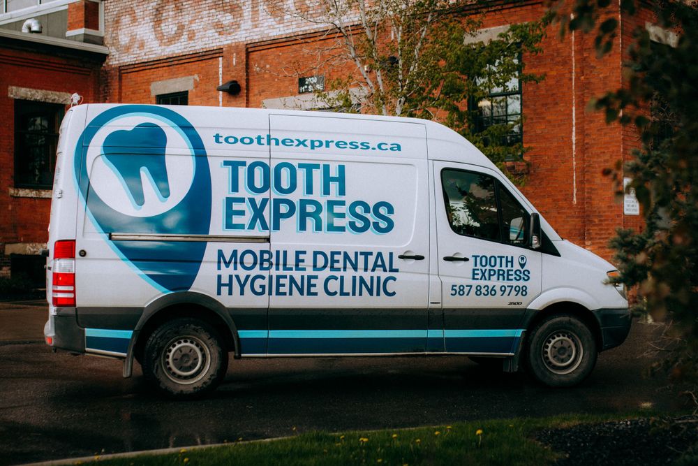 Fleet of white mobile dental hygiene clinic vans parked in front of a brick building.