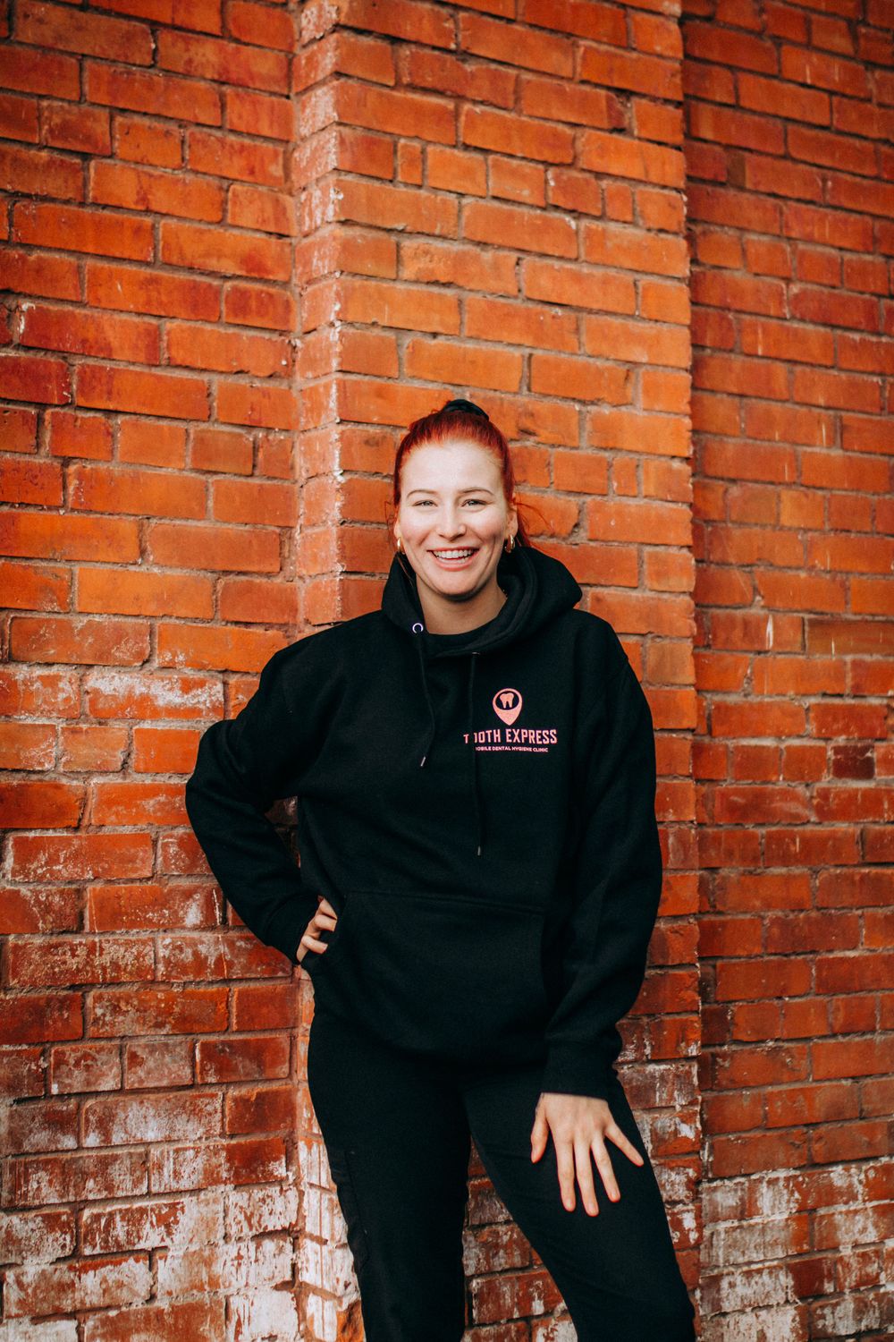 Group wearing black hoodies posing against red brick wall.