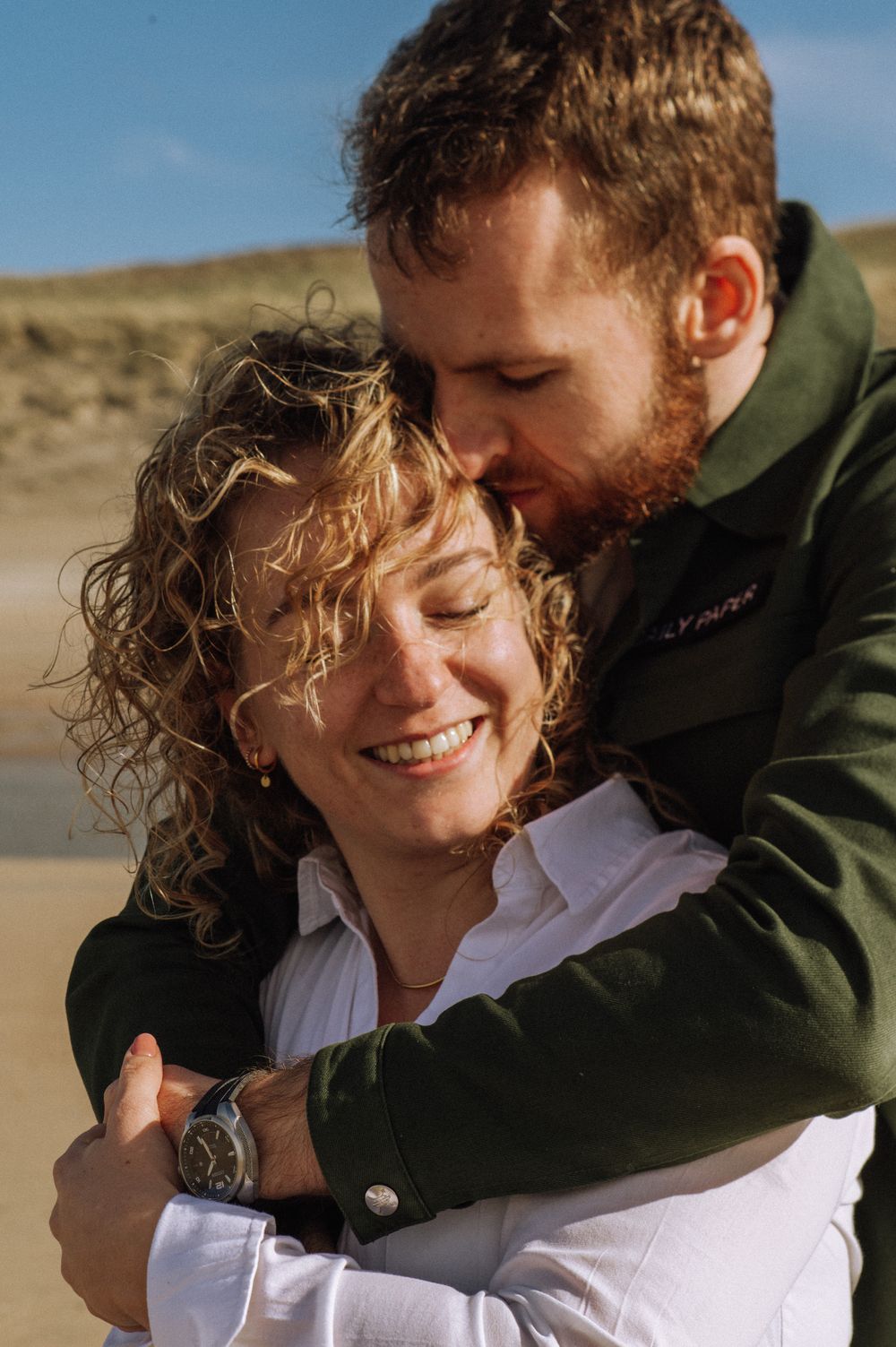 A tender embrace captured on a sandy beach with warm natural lighting.