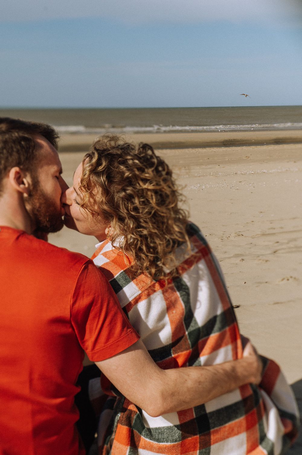 A romantic moment shared between two people on a windswept beach.