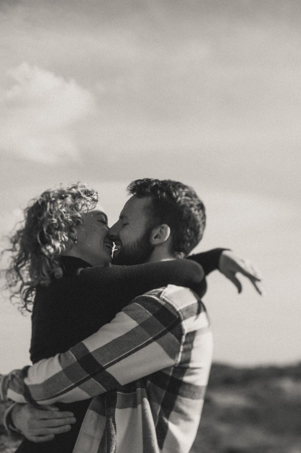 A silhouetted embrace against a cloudy sky in black and white.
