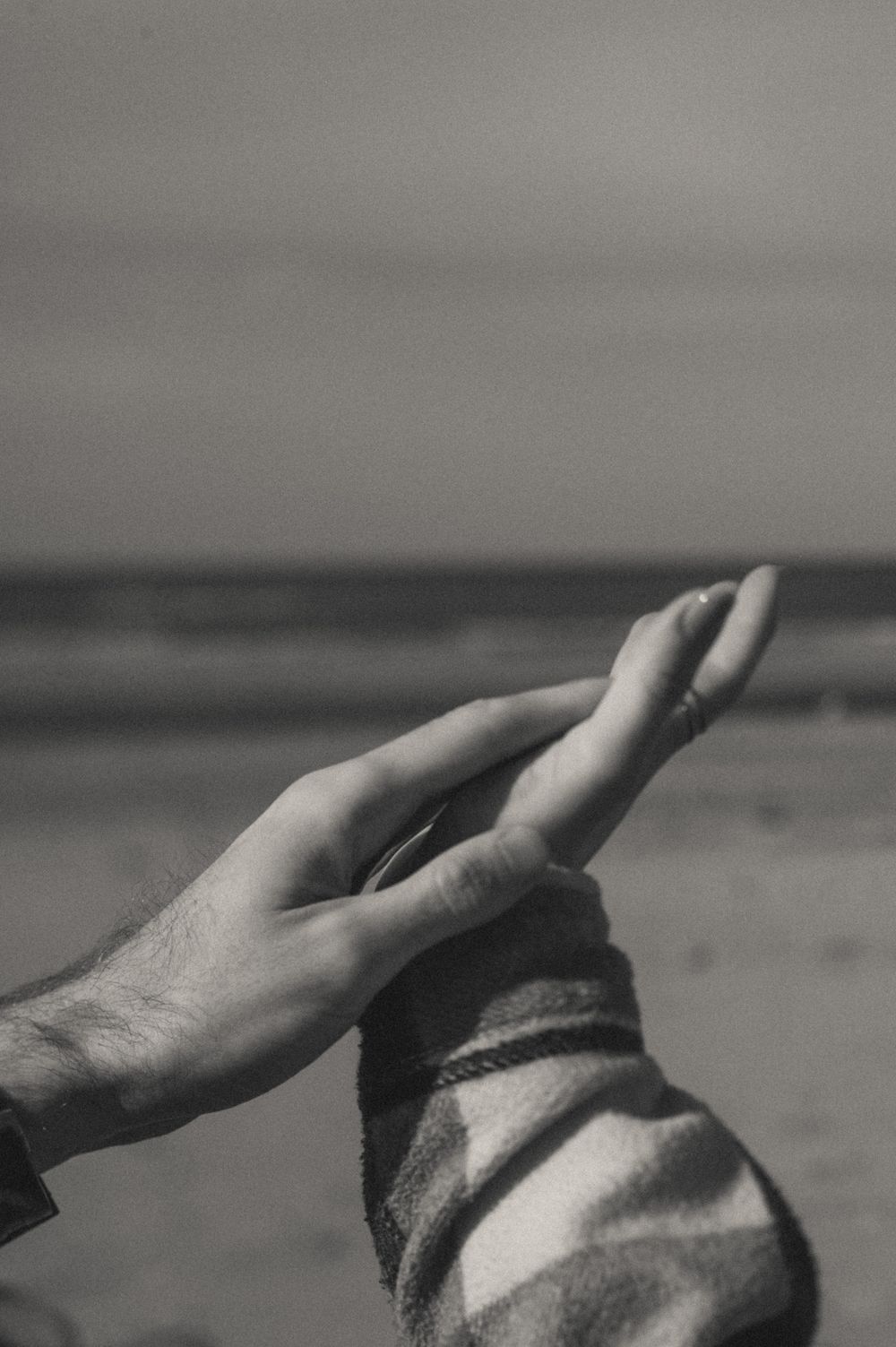 Two hands reaching toward each other against a moody beach background in black and white.