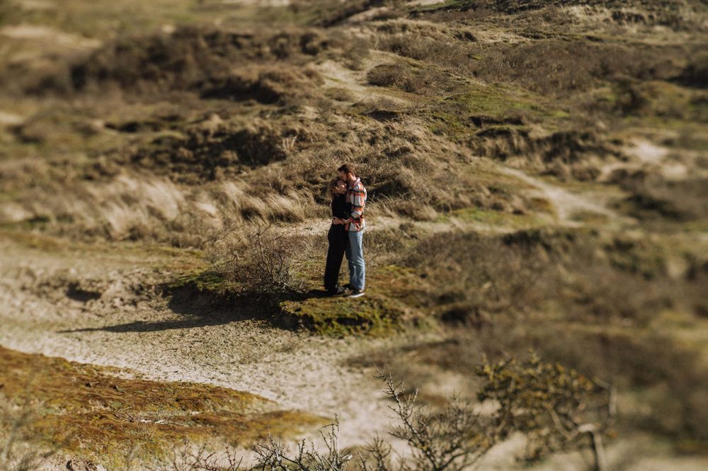 Couple embracing in a scenic coastal landscape with rolling hills and blue skies.