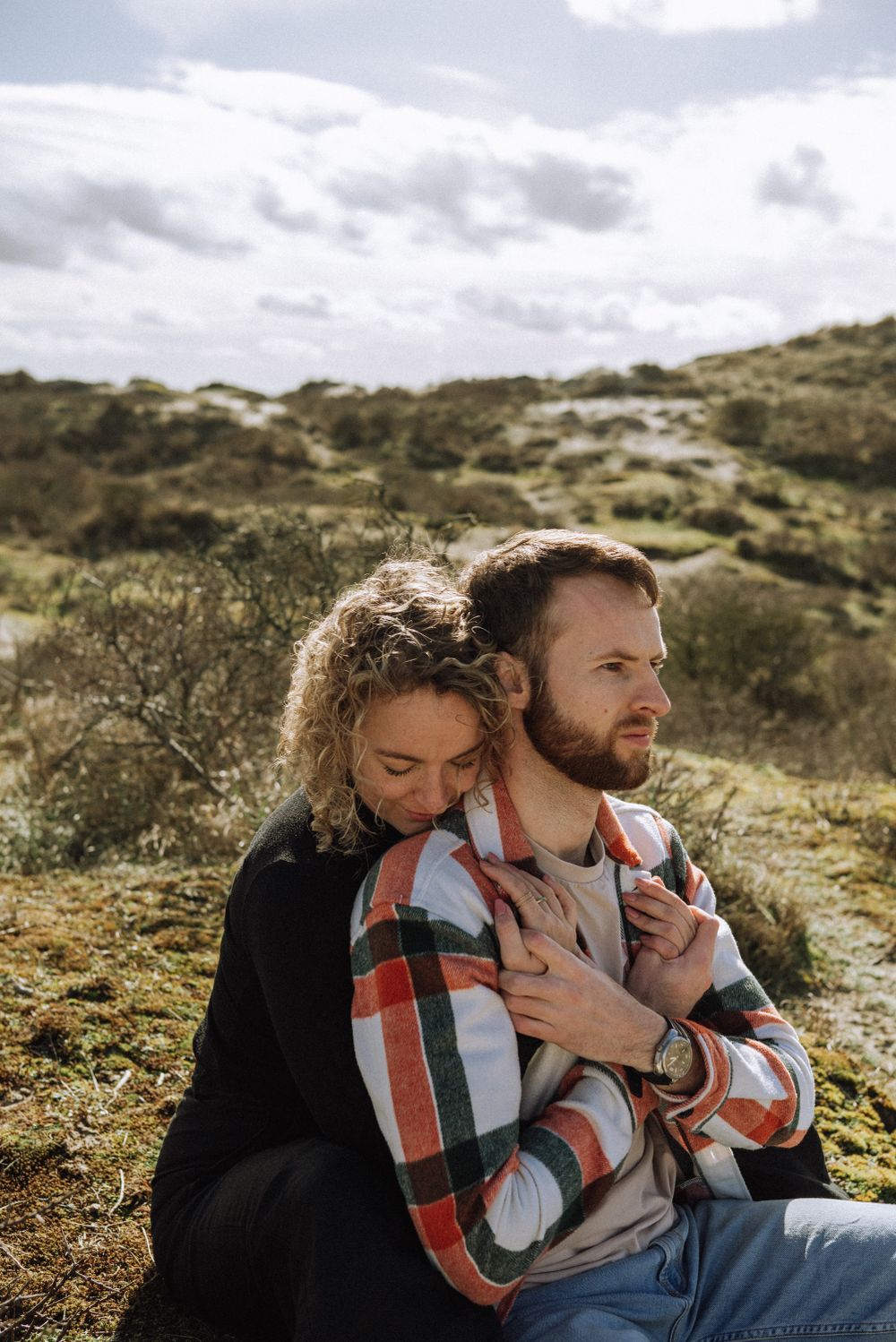 Tender embrace captured in a rugged outdoor setting with hills and vegetation.