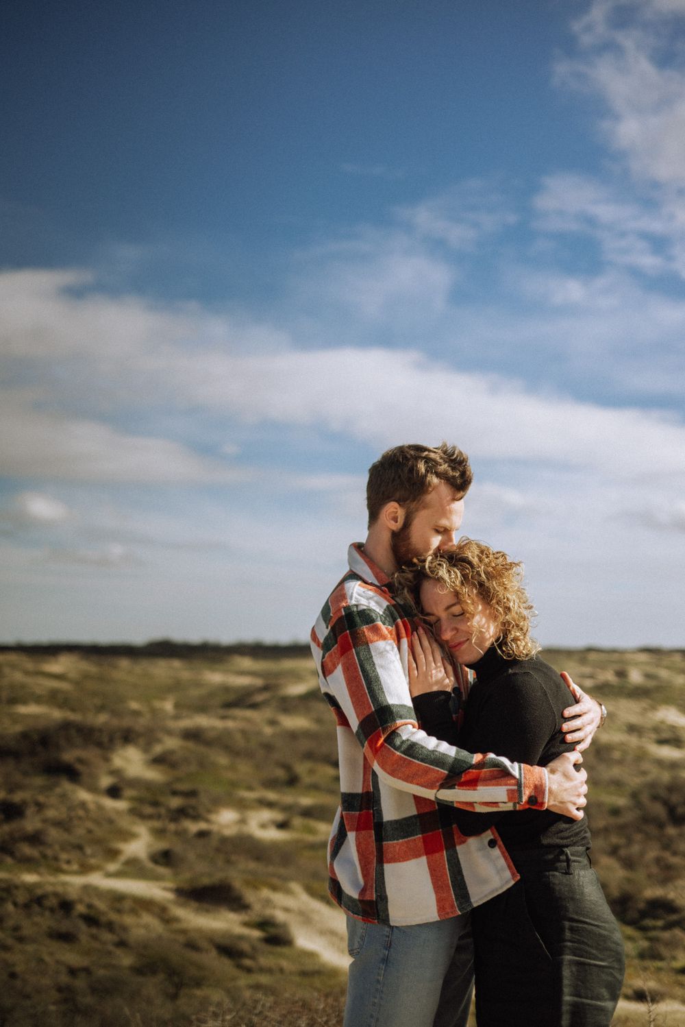 Loving embrace photographed against rolling hills and blue sky backdrop.