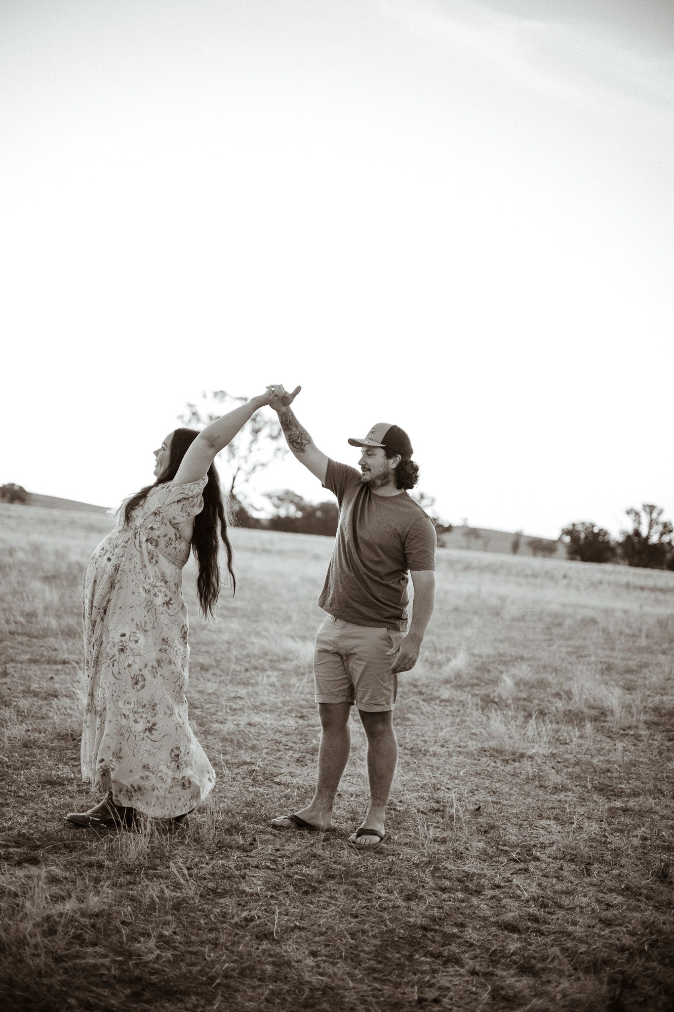Black and white photo of a couple dancing together in a grassy field at sunset.