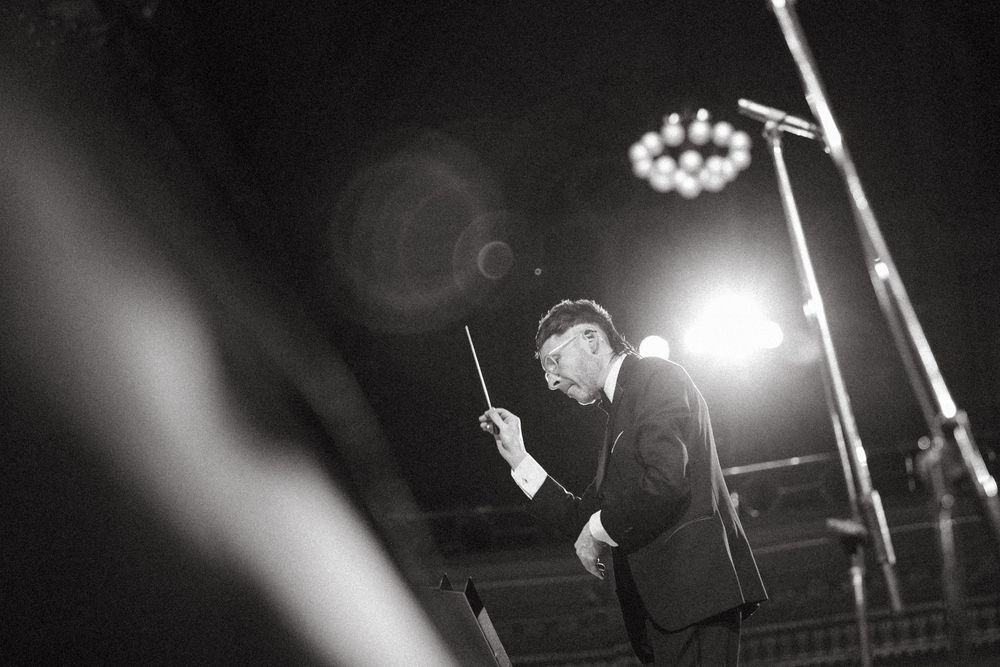 A dramatic black and white concert photo shows a performer silhouetted against bright stage lights.