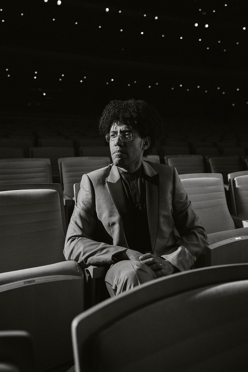 A person sits alone in dark theater seats, shown in a dramatic black and white composition.
