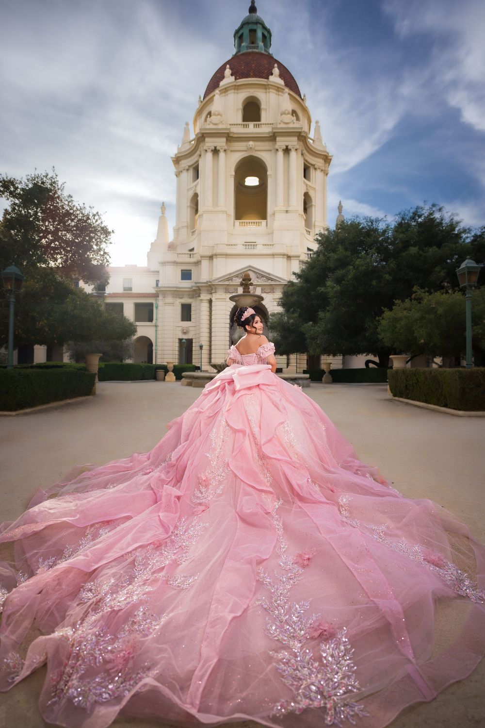 A pink quinceañera dress with a flowing tulle skirt photographed in front of the Pasadena City Hall dome.