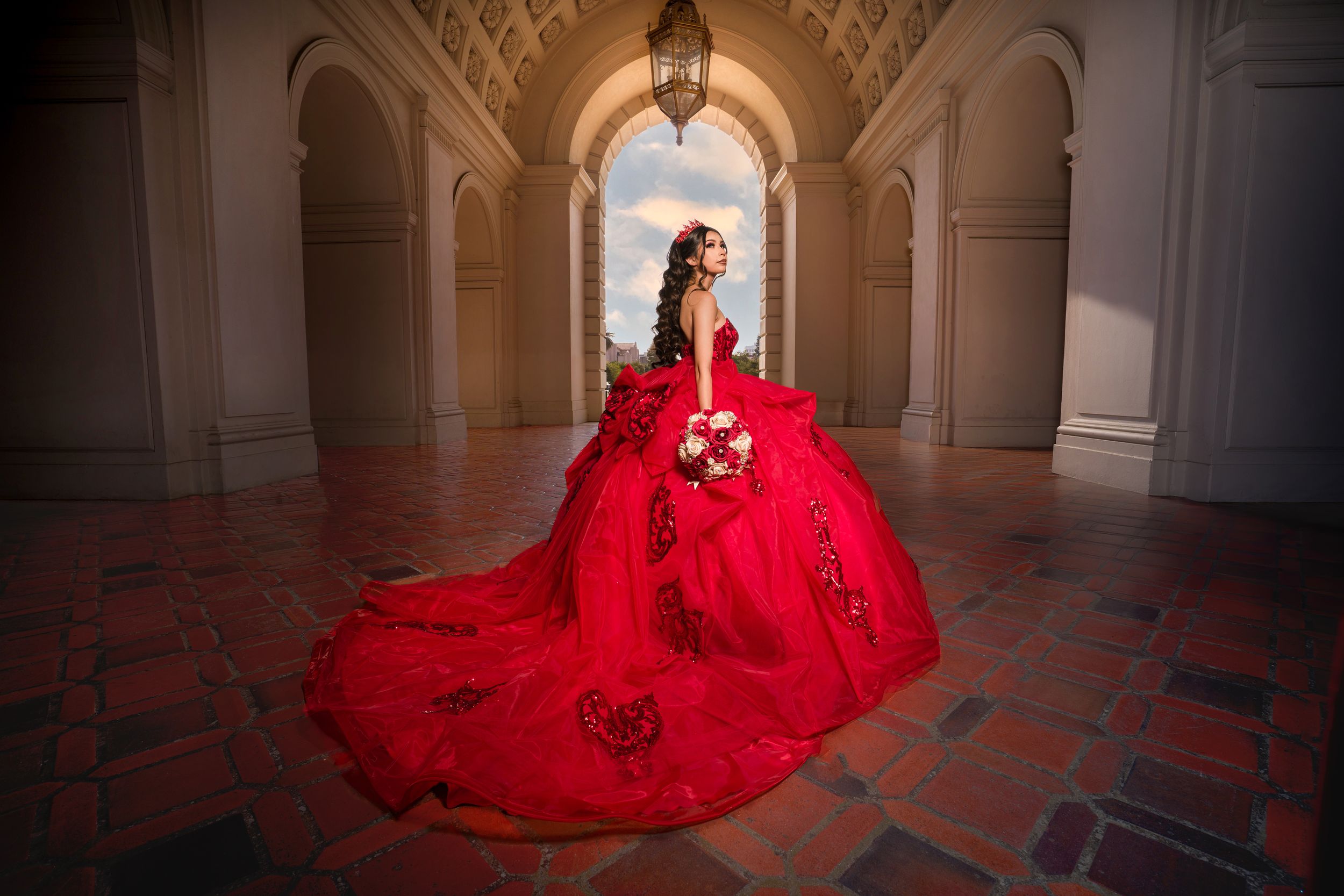 A figure in a flowing red gown stands gracefully in an elegant arched hallway with ornate architecture.