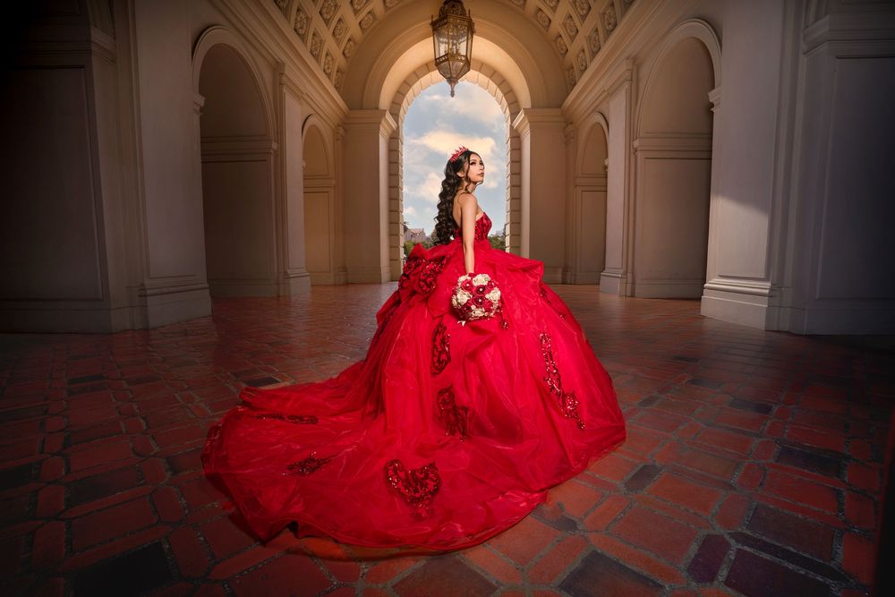 A figure in a flowing red gown stands gracefully in an elegant arched hallway with ornate architecture.