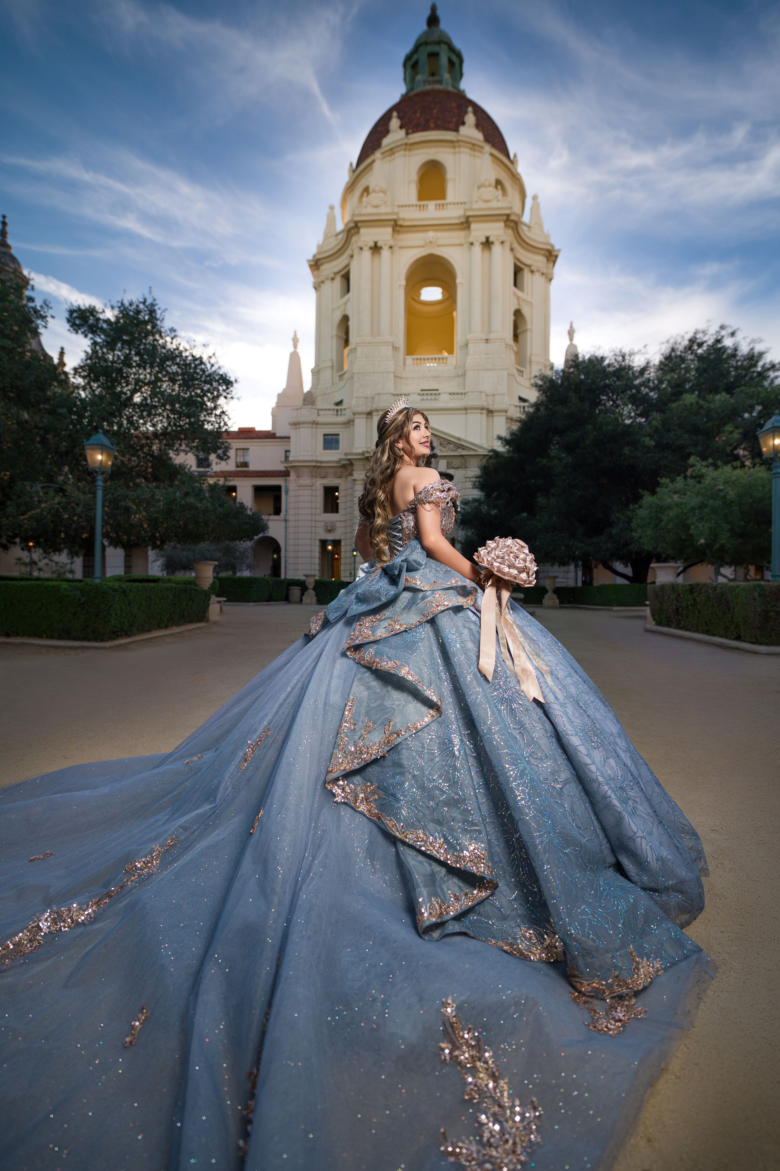 A stunning blue ballgown with gold embellishments photographed in front of a historic church building at sunset.