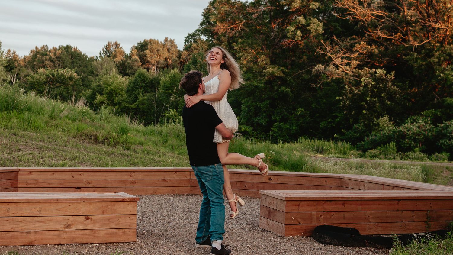 A joyful couple embraces in front of wooden garden boxes during sunset in an outdoor setting.