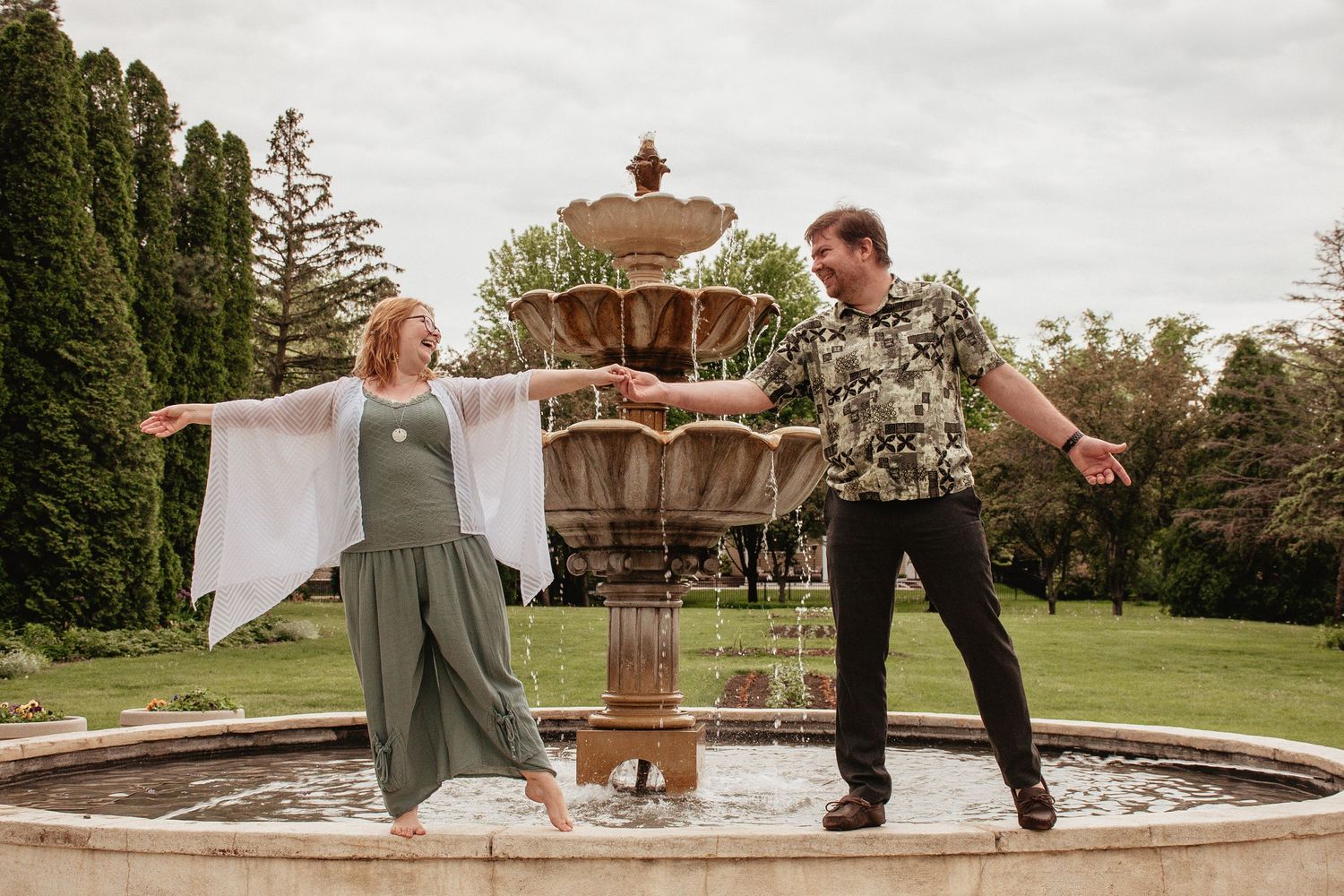 A playful couple poses near an ornate fountain in a formal garden setting.