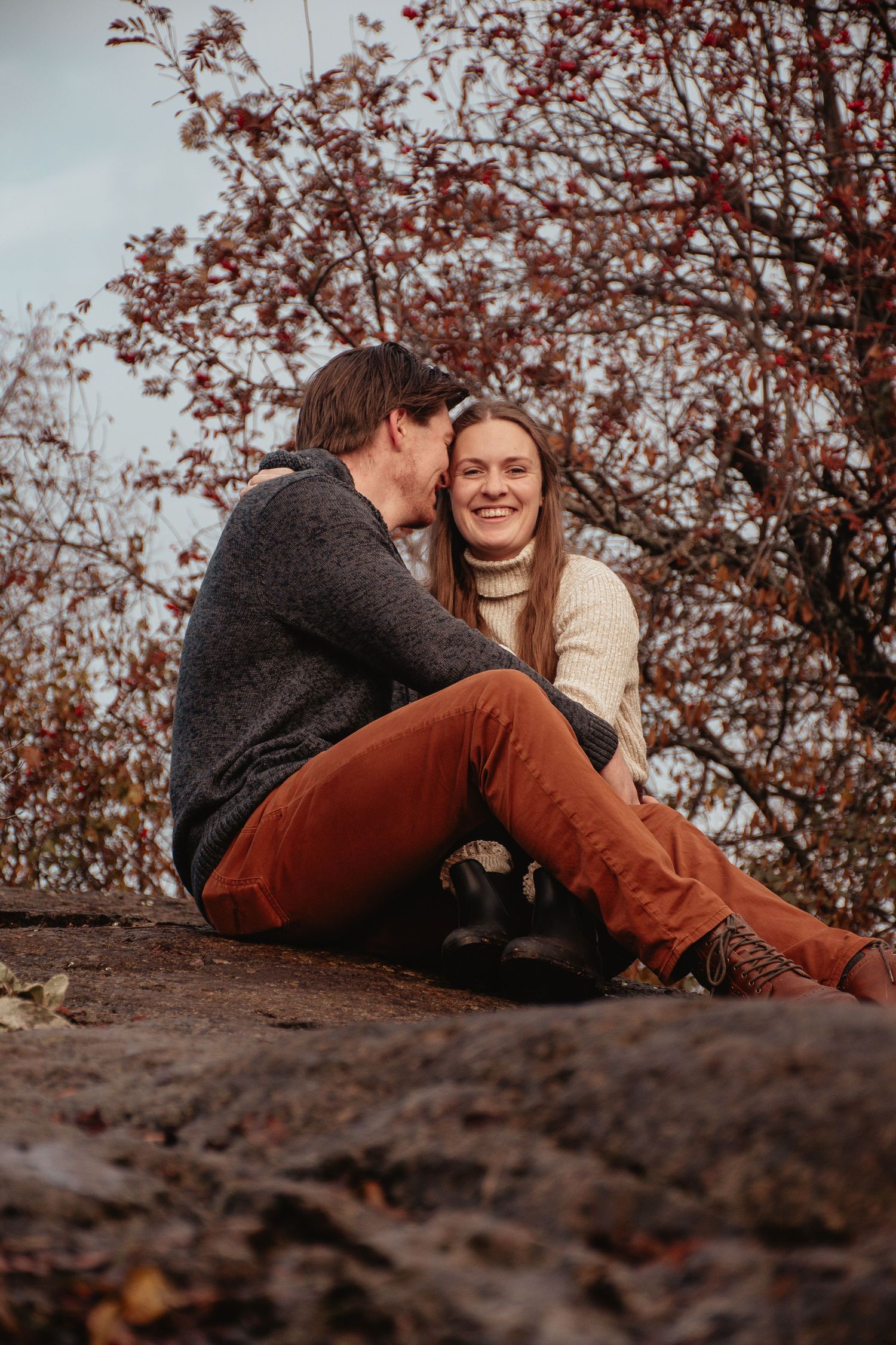 A cozy autumn scene with a couple sitting on rocks under blooming cherry trees.
