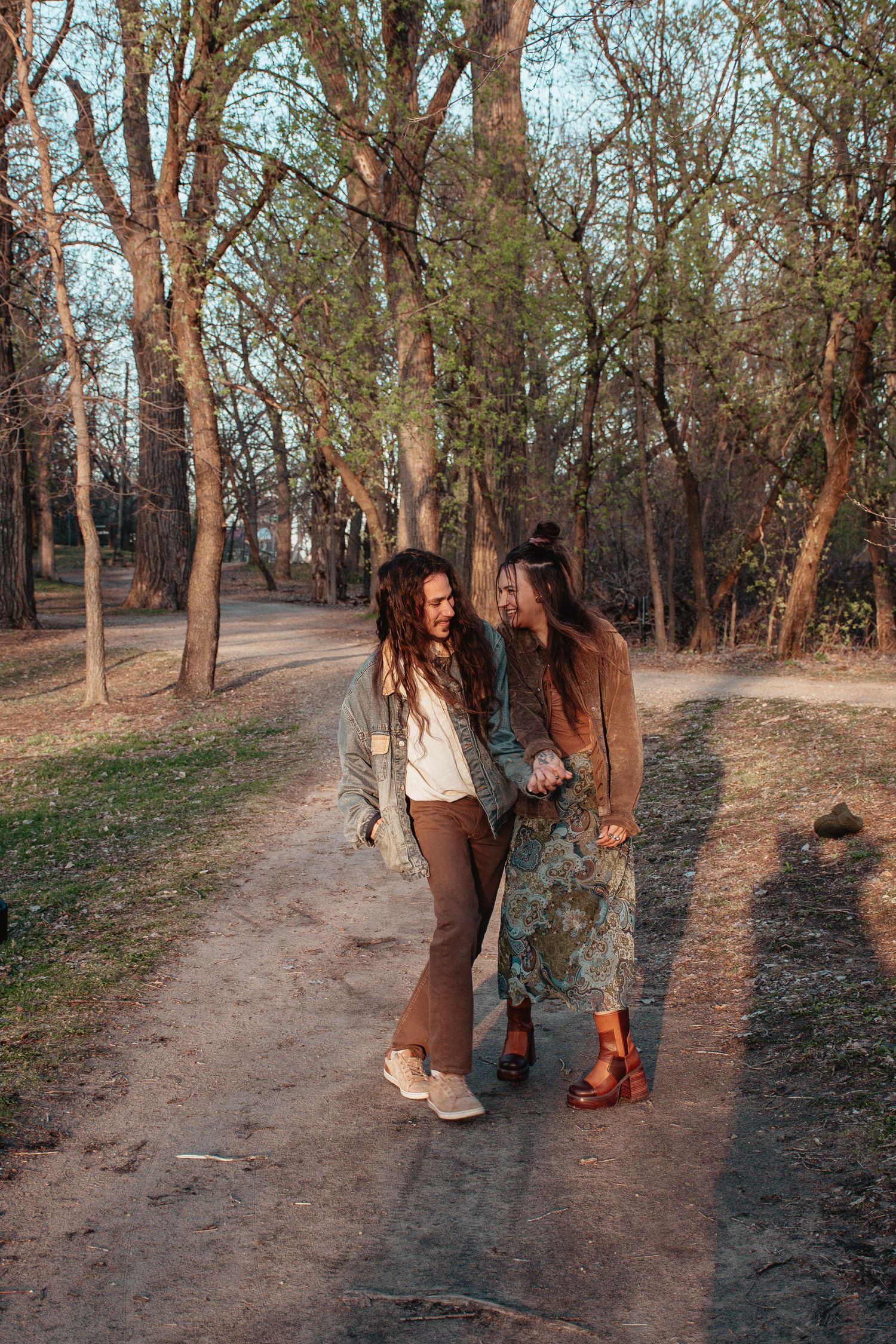Two people sharing a romantic walk on a wooded trail during golden hour.