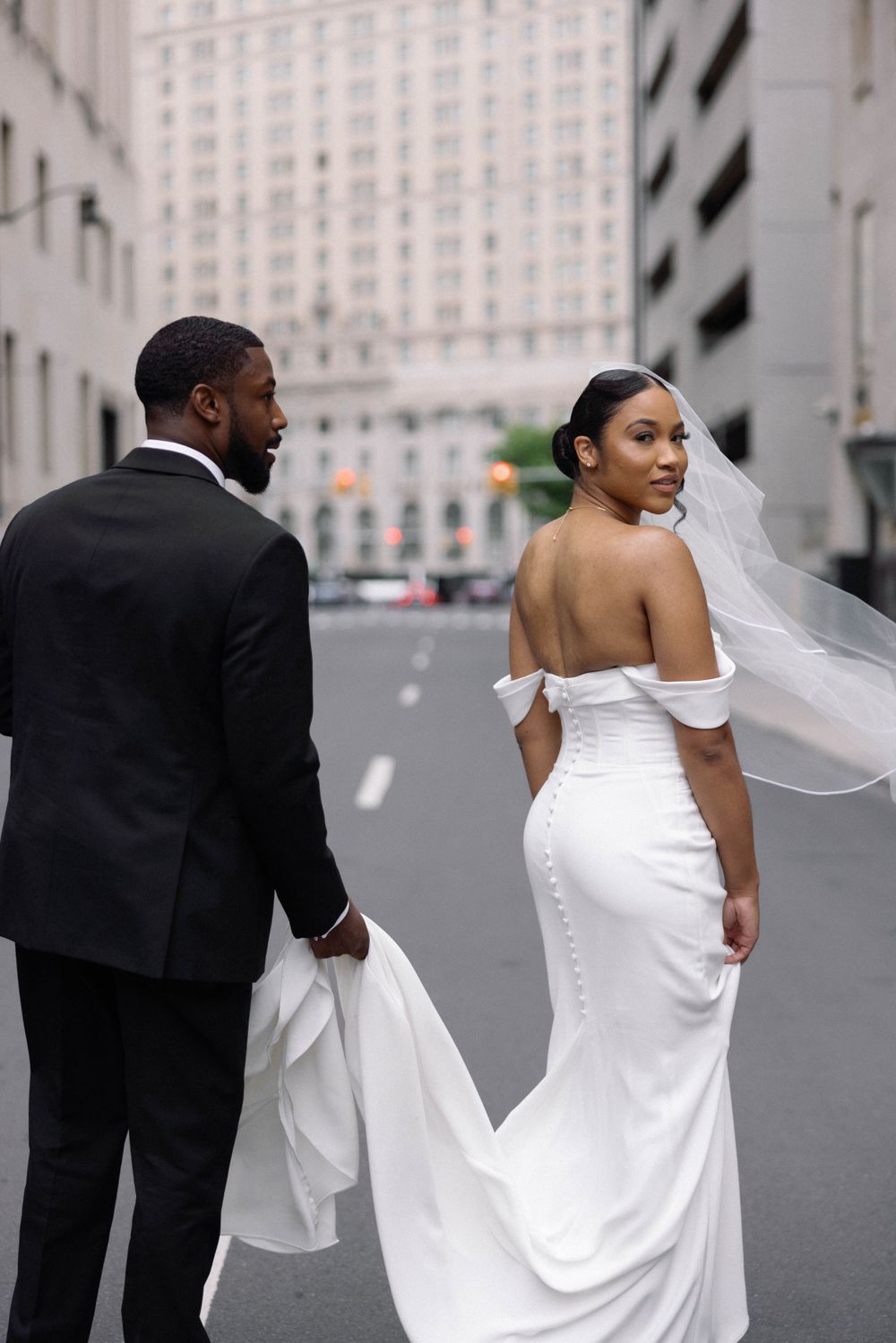 Elegant couple in wedding attire walking down urban street.