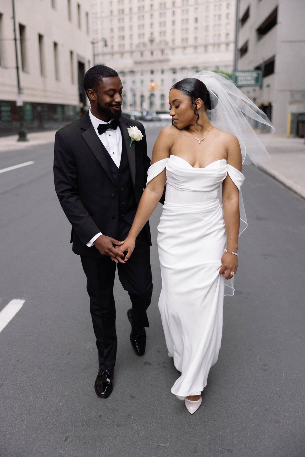 Couple shares romantic moment while walking down city street in wedding attire.