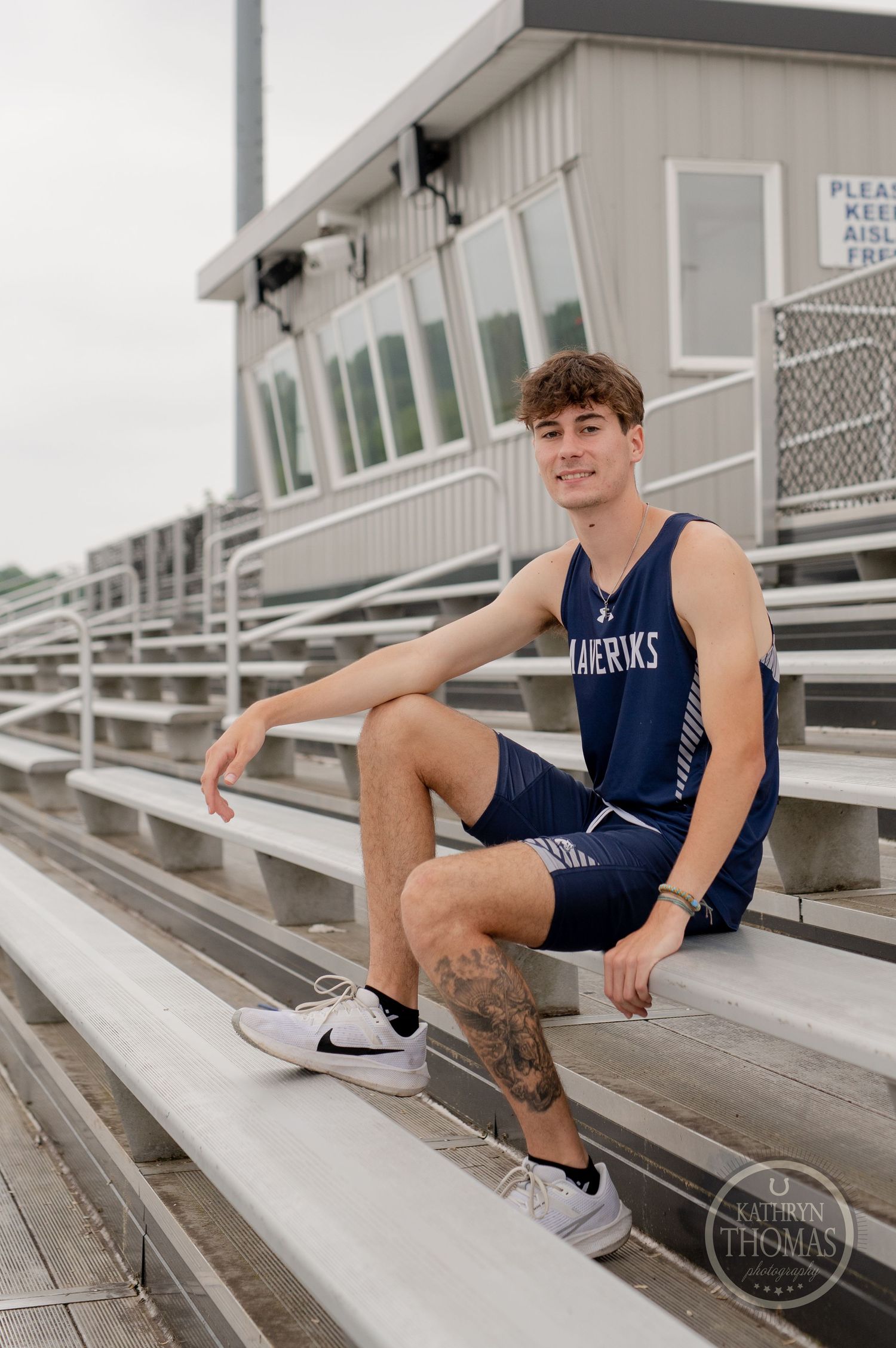 Student athlete in Mavericks uniform poses on stadium bleachers.