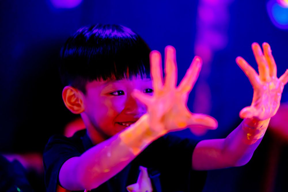 Person gesturing under dramatic neon lighting with blue and pink colors.