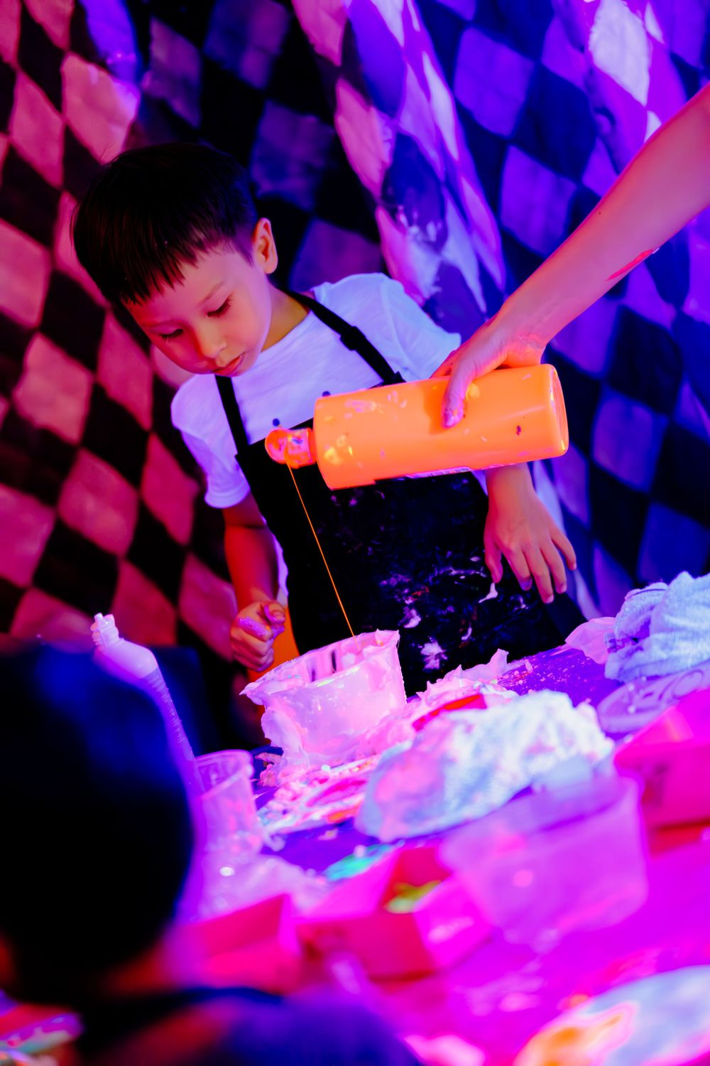 Young person pouring liquid at table decorated with neon colors and patterns.