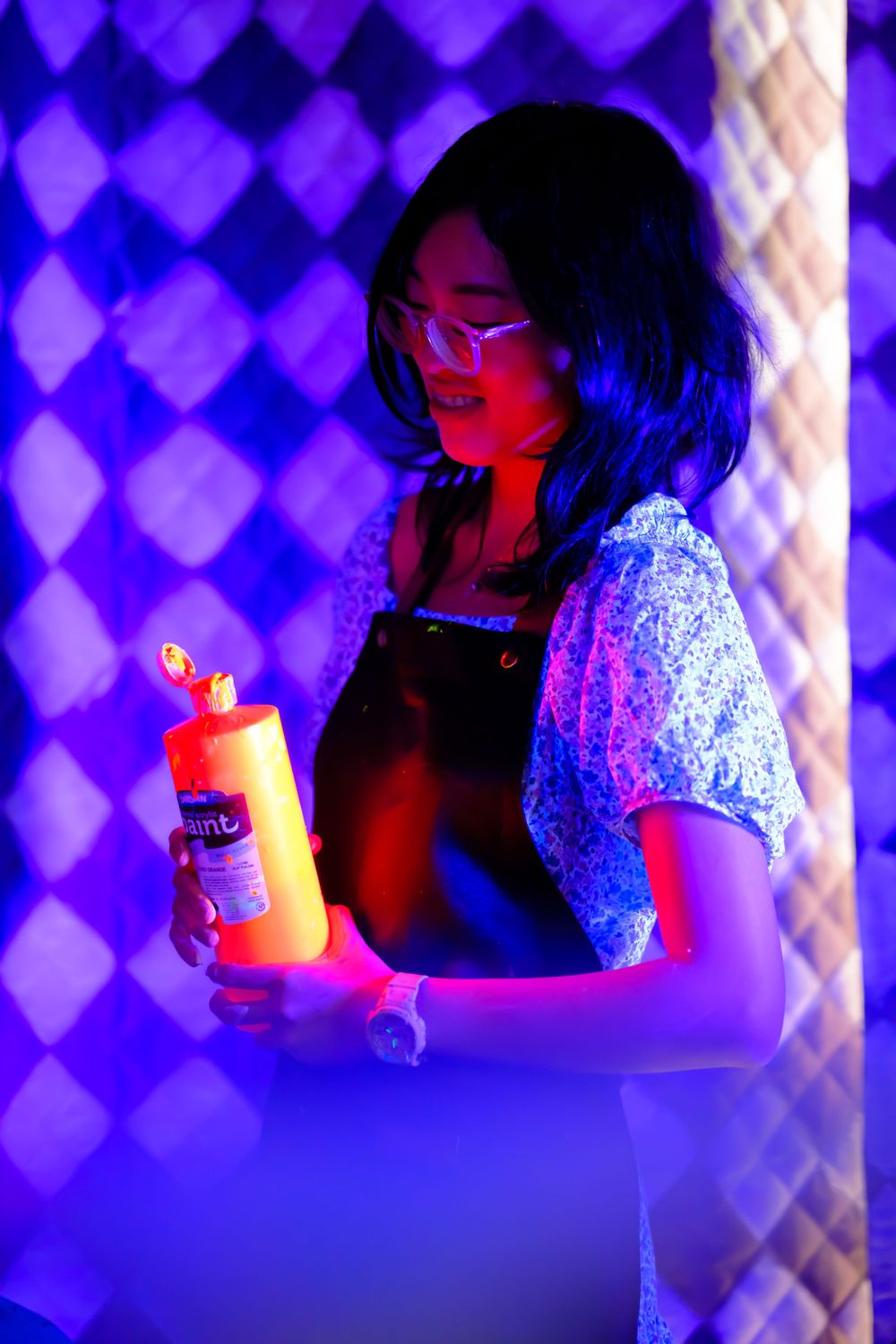 Person holds glowing bottle against geometric purple patterned background.