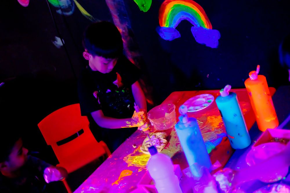Party setup with rainbow decorations and neon-colored bottles under blacklight.