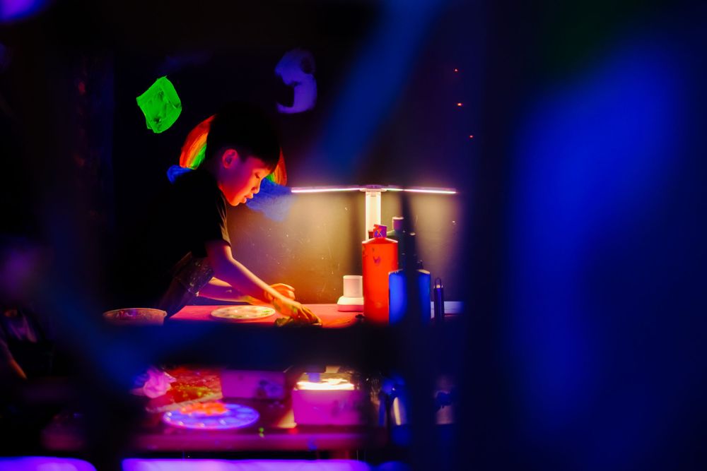 Person working at table illuminated by colorful neon lights and decorative elements.