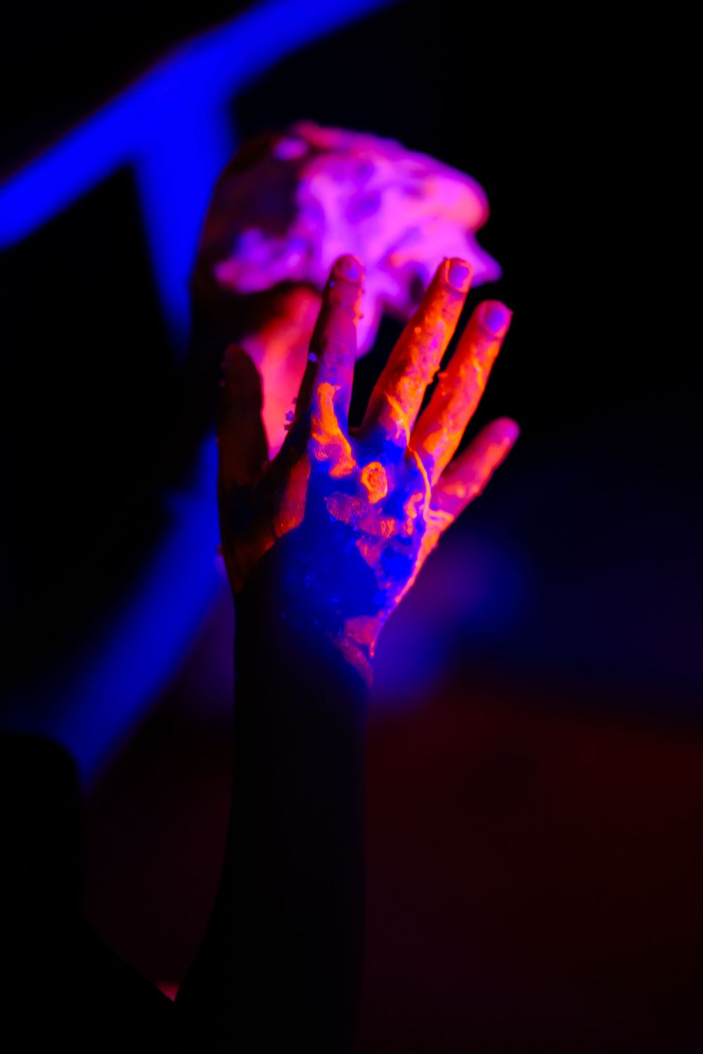 Hand illuminated by neon pink and blue ultraviolet lights creating dramatic contrast against dark background.