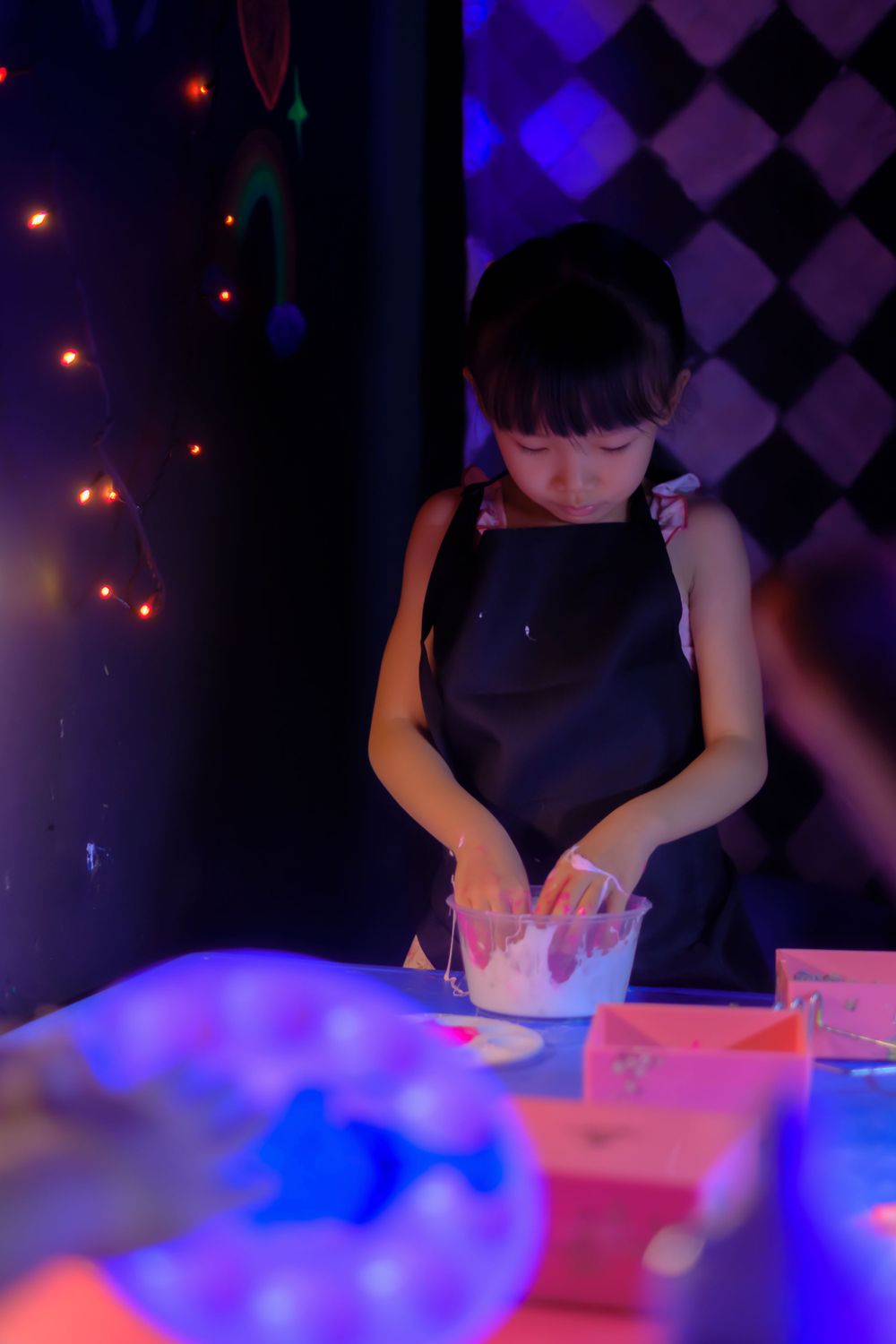 Person working with glowing materials at dark table with blue ambient lighting.