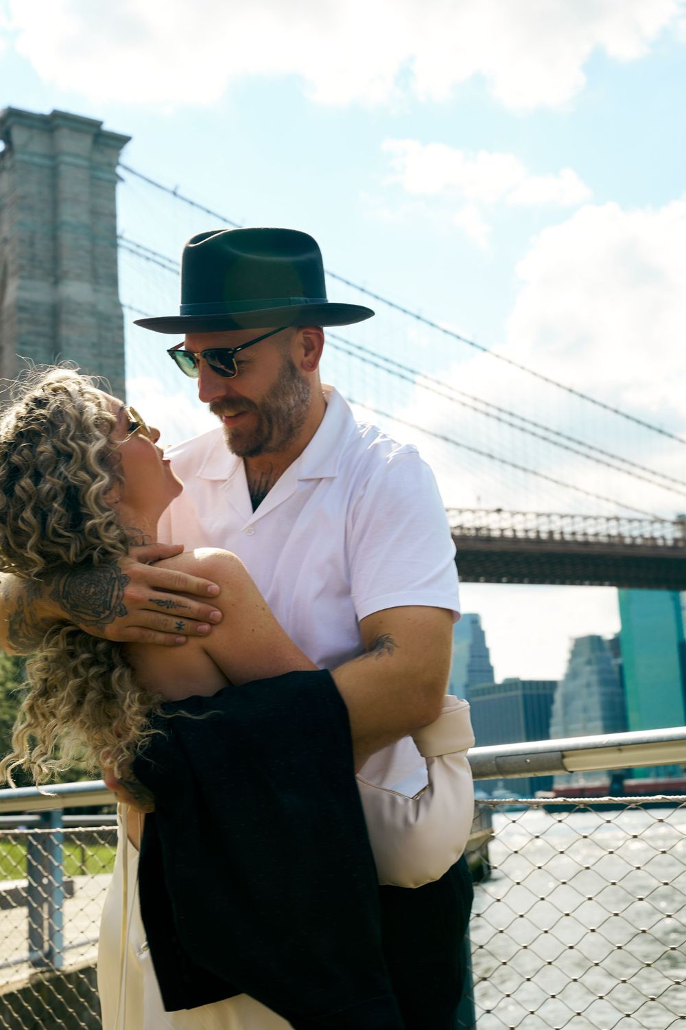 Romantic couple embracing by Brooklyn Bridge with NYC skyline in background.
