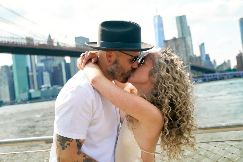 Couple sharing intimate moment near Brooklyn Bridge with Manhattan skyline in background.