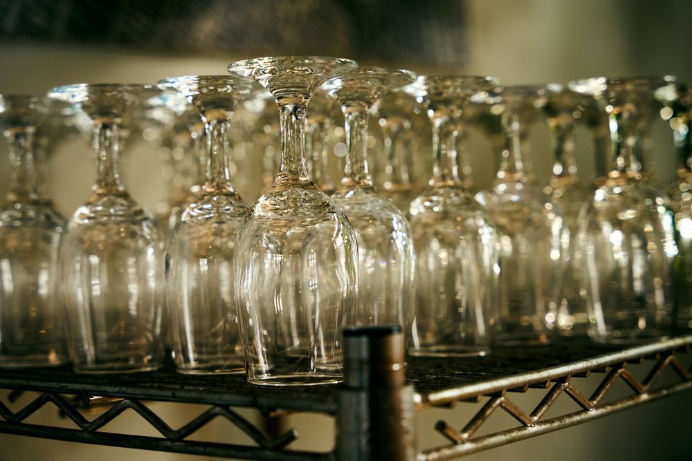 Rows of empty wine glasses arranged on a metal rack shelf with soft lighting and bokeh effects.
