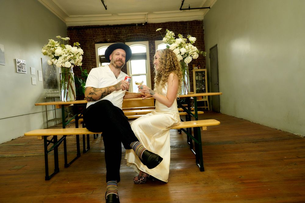 A couple shares a playful moment in an industrial-style room decorated with floral arrangements.