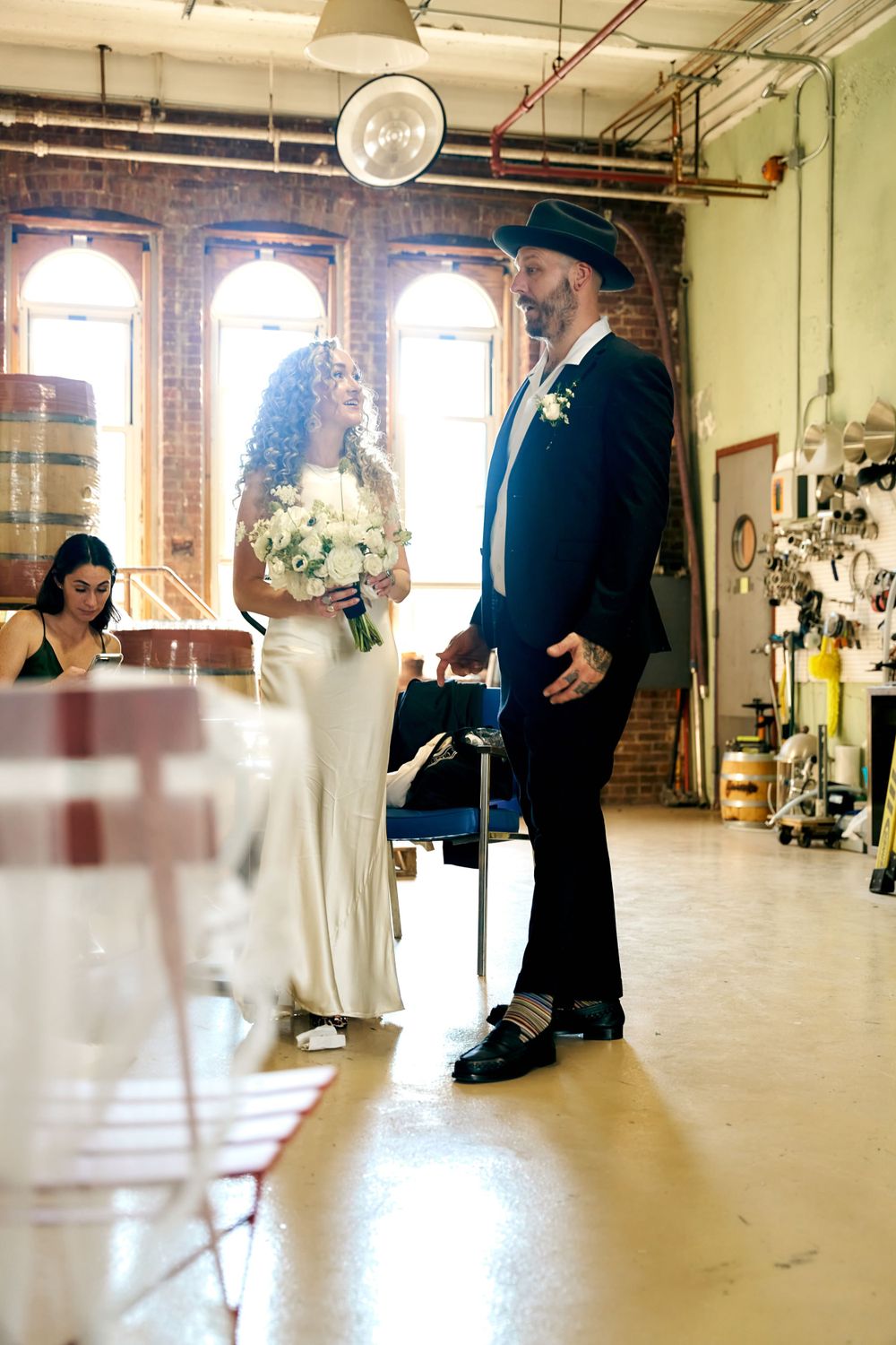 A wedding ceremony in a rustic brick-walled venue with arched windows and industrial details.