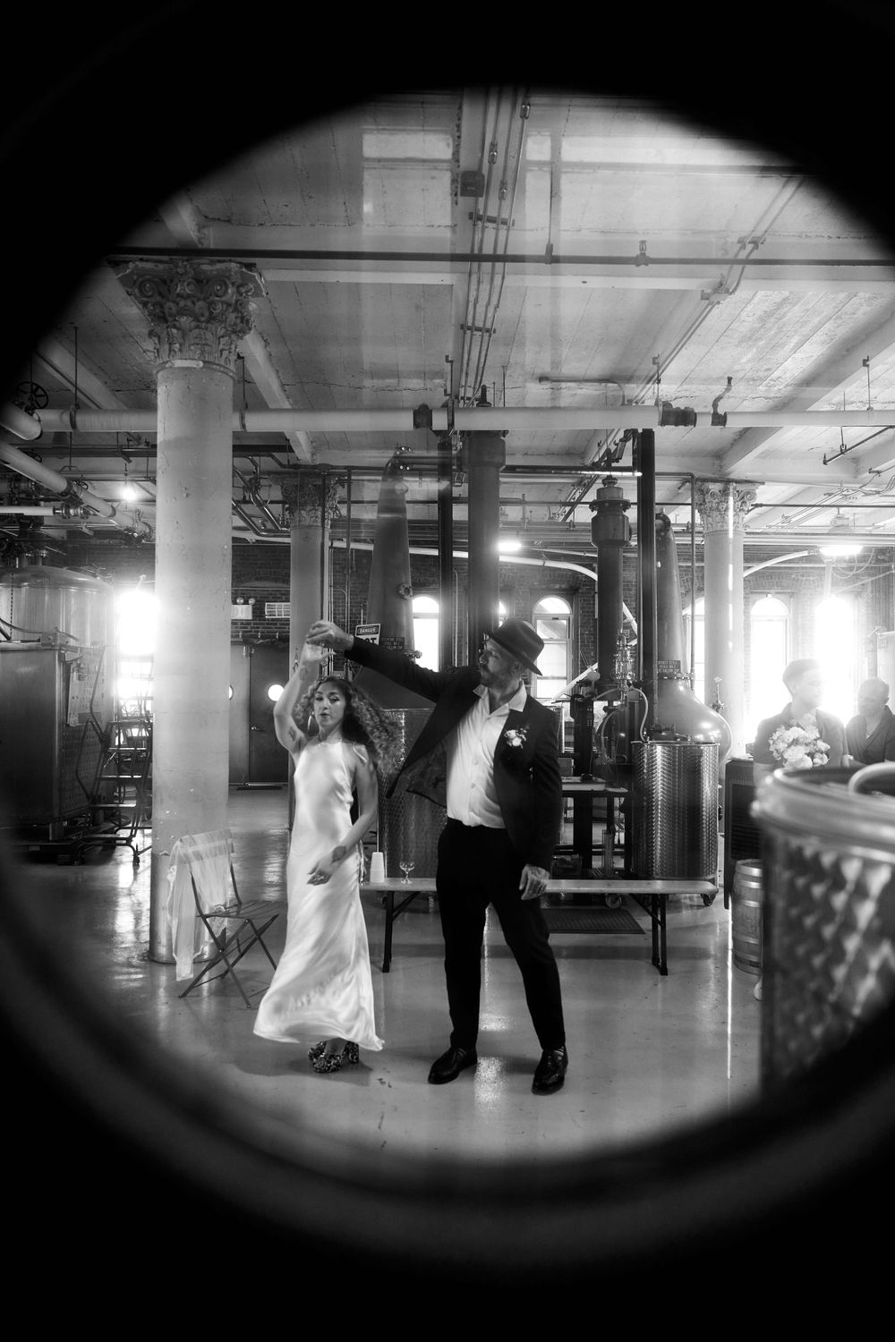 A black and white shot of a dancing couple in an industrial venue viewed through a circular frame.