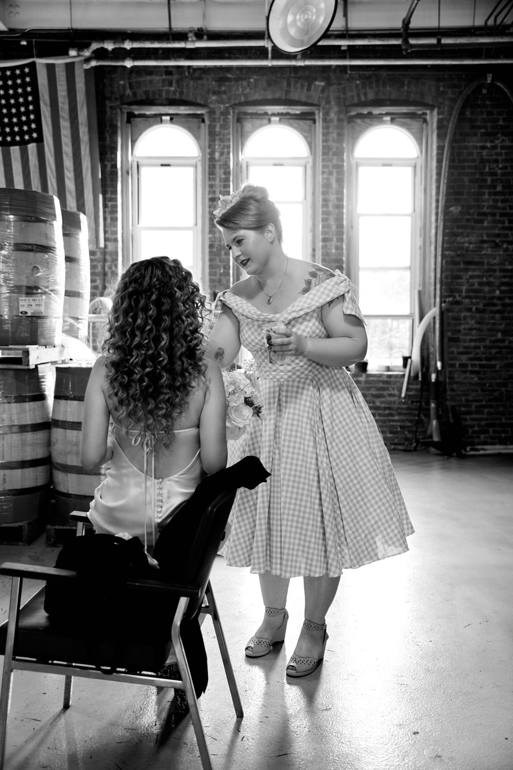 A black and white photo of wedding preparations in a rustic venue with arched windows.