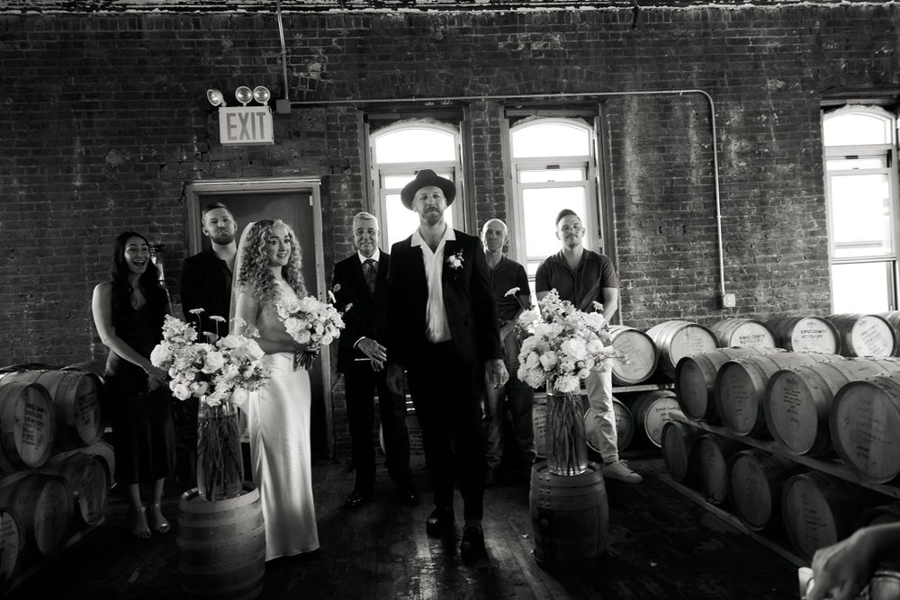 A black and white wedding photo in an industrial venue with wooden barrels and exposed brick walls.
