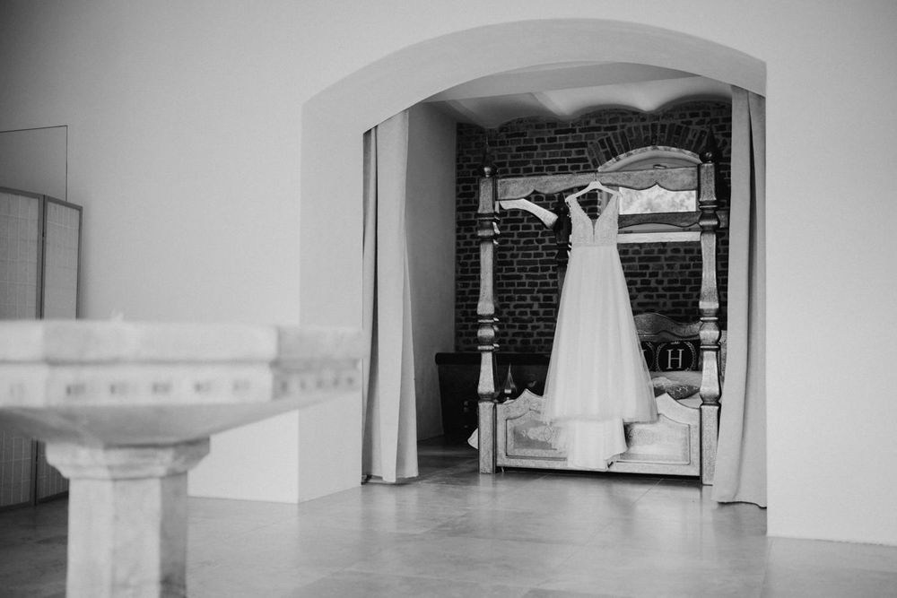 Black and white photo of a wedding dress displayed in an arched doorway with brick walls.