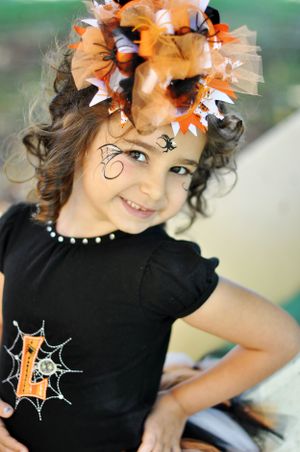 A child in Halloween costume wearing a black shirt with spiderweb design and orange ribbon hair accessory.