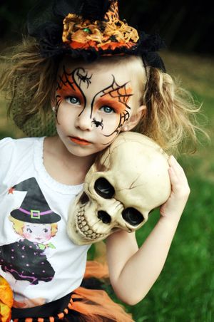 Halloween makeup with orange spiderweb design holding decorative skull.